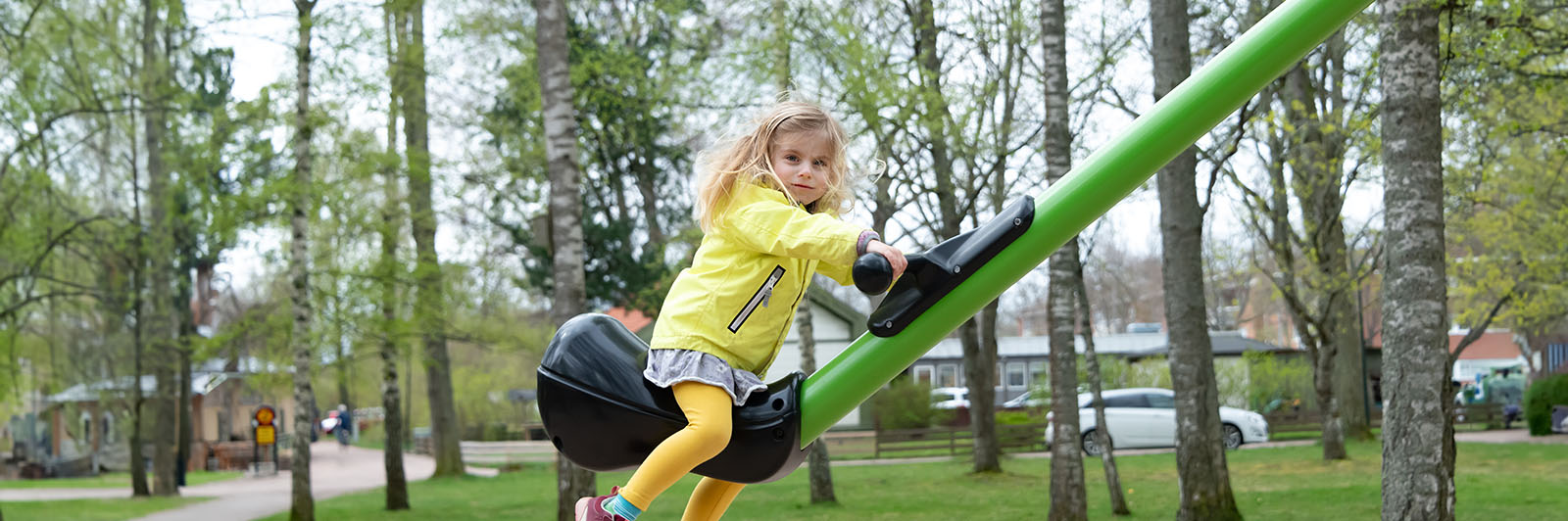 A young girl in a yellow coat plays on a playground seesaw.